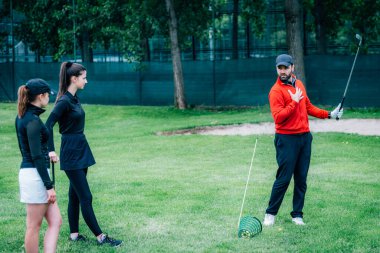Golf dersi. Golf hocası genç kadınlara salıncak tekniği gösteriyor