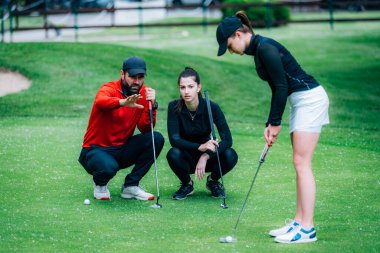 Golf dersi, golf hocasıyla golf antrenmanı yapan iki genç bayan golfçü.