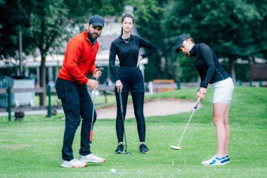 Golf dersi, golf hocasıyla golf antrenmanı yapan iki genç bayan golfçü.