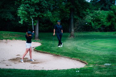 Golf ve kum tatbikatı. Genç kadın golf hocasından ders alıyor.