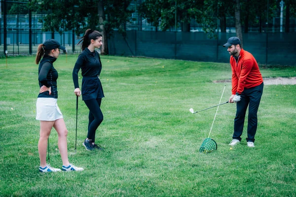 Golf dersi. Golf hocası genç kadınlara salıncak tekniği gösteriyor