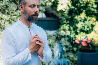 Bir adam dışarıda meditasyon yapar ve dua pozisyonunda el ele tutuşur..  