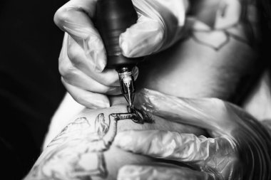 Plastik eldivenli bir el elektrikli dövme tabancasıyla dövme çiziyor.