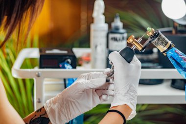 Kadın dövme sanatçısı, erkek koluna dövme yapmak için dövme makinesi hazırlıyor. 