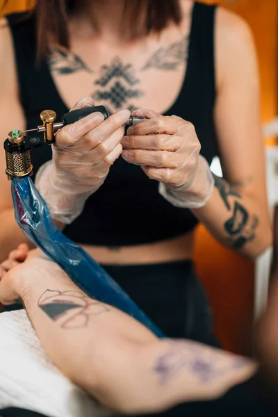 Kobieta Tatuażystka Przygotowuje Maszynę Tatuażu Ramieniu Mężczyzny — Zdjęcie stockowe