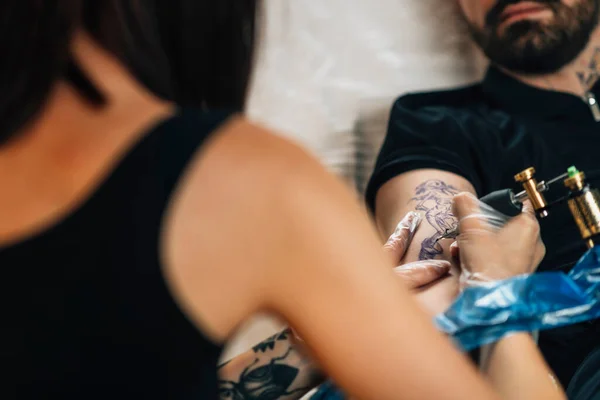 Female tattoo artist tattooing mans arm in studio