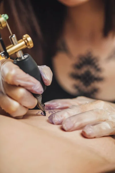 Hand of tattooist in rubber gloves drawing a tattoo with electric tattoo gun, close-up