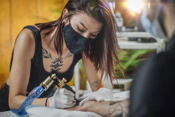 コロナウイルス危機時の安全性の確保 タトゥーアーティストは Covid 19パンデミック時にタトゥースタジオで手袋とフェイスマスクでクライアントを入れ墨 — ストック写真