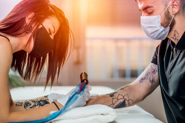 Professional female tattoo master applying tattoo on hand of young man with tattoo machine