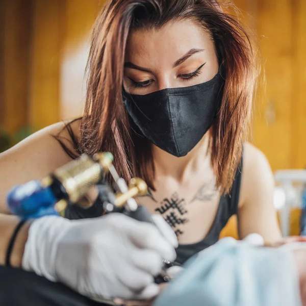 コロナウイルス危機時の安全性の確保 タトゥーアーティストは Covid 19パンデミック時にタトゥースタジオで手袋とフェイスマスクでクライアントを入れ墨 — ストック写真