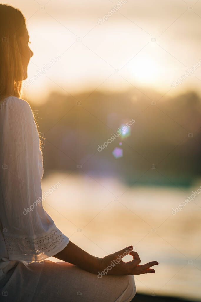 Sungazing. Woman meditating by the lake, sitting in lotus position.  