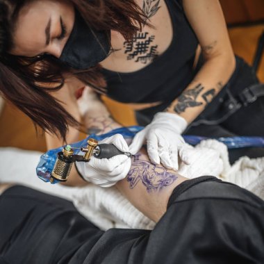 Dövme ustası bir kadının stüdyoda kolunu dövmesinin en üst görüntüsü. 