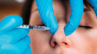 Deri dolguları tedavi görüyor. Deri doldurucu yüz enjeksiyonları için kadınların burun köprüsünü şekillendiren doktor.. 