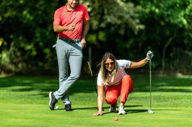 Golf oynayan bir çift, yeşil okuyan genç bir kadın, golf oynamaya hazırlanıyor.