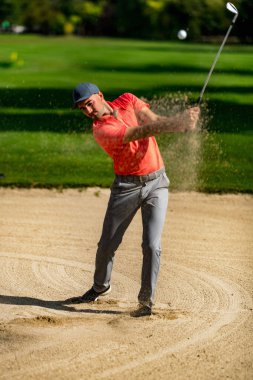 Kumdan golf atışı, profesyonel golfçü kum deposundan oynuyor, havada golf topu var.