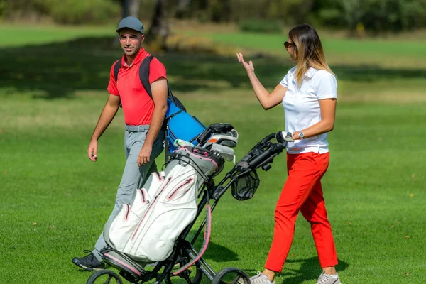 Genç çift golf oynamaktan zevk alıyor. Güneşli bir günde golf sahasında yürüyorlar.