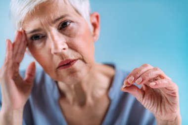 Migren ilacı. Migren ağrısı olan yaşlı bir kadın elinde ağrı kesici bir hap tutuyor. Bir hapla eline odaklan..
