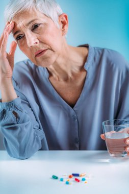 Migren ağrısı olan yaşlı bir kadın. İçinde haplar ve bardaklar vardı..