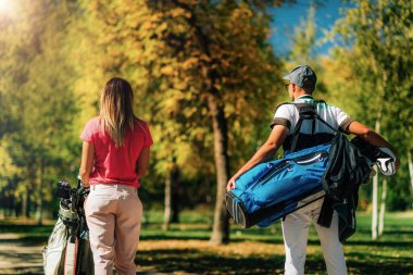 Golfçü çift, bir sonraki deliğe doğru yürüyorlar, arkadan çekiliyorlar, güzel sonbahar havası.