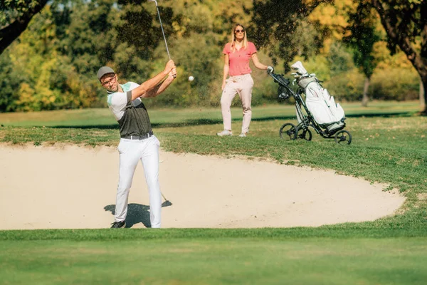 ゴルフをするカップル砂のバンカーから出てくるゴルファー — ストック写真