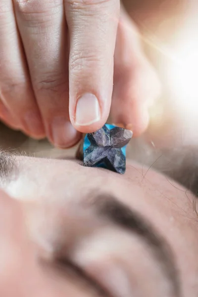 Healing crystal. Young man with Merkaba crystal placed on his forehead on third eye\'s area.