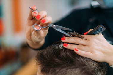 Little boy getting his hair cut by a female hairdresser in a hair salon for children.