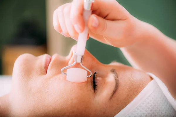 Guasha face massage in beauty salon, massage technique for stimulating pressure points on the face, using jade stone roller