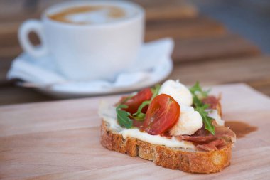 Rahatlatıcı kahvaltı için lezzetli rustik sandviç - tam tahıllı ekmek, jambon, mozzarella peyniri, roka, domates ve bir fincan lezzetli kapuçino kahvesi