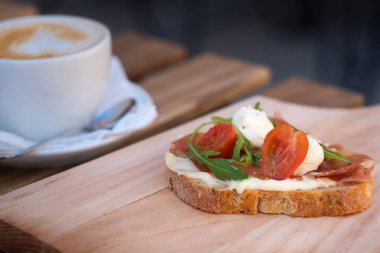 Rahatlatıcı kahvaltı için lezzetli rustik sandviç - tam tahıllı ekmek, jambon, mozzarella peyniri, roka, domates ve bir fincan lezzetli kapuçino kahvesi