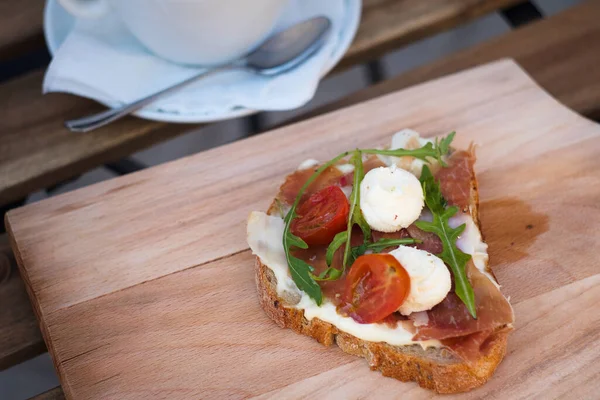 Rahatlatıcı kahvaltı için lezzetli rustik sandviç - tam tahıllı ekmek, jambon, mozzarella peyniri, roka, domates ve bir fincan lezzetli kapuçino kahvesi