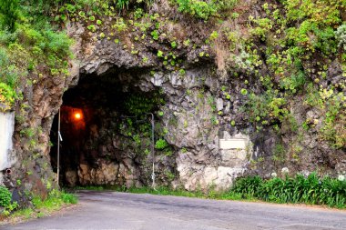 Portekiz 'in Madeira adasının batı kıyısındaki doğal mağara tünelinde kıvrılan manzaralı asfalt karayolu.