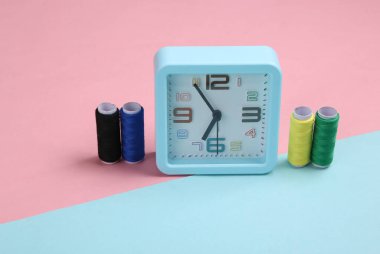 Mavi-pembe pastel arka planda renkli ipliklerin derisi olan çalar saat. Hobi zamanı