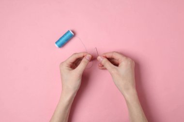 Kadın elleri iğneyi ipliğe geçirir ve dikiş dikmeye hazırlanır.