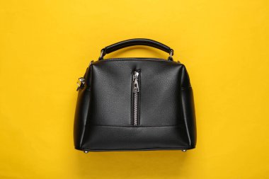 Sarı arka planda siyah deri bir çanta. Üst görünüm