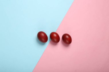 Mavi-pembe pastel arka planda kırmızı paskalya yumurtaları boyadım. Paskalya minimalist kompozisyonu. Üst görünüm