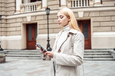 Şehirde akıllı telefon kullanan genç sarışın kadın.