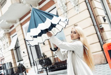 Genç sarışın kadın yağmur beklentisiyle şehirde şemsiye açıyor