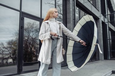 Genç moda kadını iş merkezinin yanında şemsiye açıyor.
