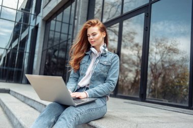 Genç bir kız öğrenci ya da serbest çalışan elinde dizüstü bilgisayarla merdivenlerde oturuyor.