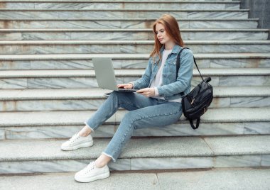 Laptoplu güzel bayan öğrenci dışarıda merdivenlerde oturuyor. Uzaklık eğitimi