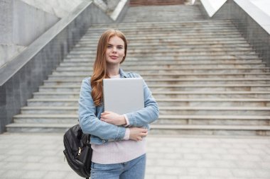 Diz üstü bilgisayarı ve sırt çantası olan, kızıl saçlı, tatlı bir kız öğrenci.