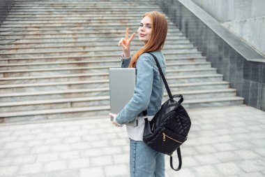 Diz üstü bilgisayarı ve sırt çantası olan, kızıl saçlı, tatlı bir kız öğrenci.
