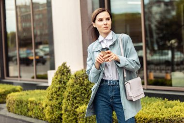 Trençkotlu iş kadını şehirde giderken kahve içer. Yaşam biçimi