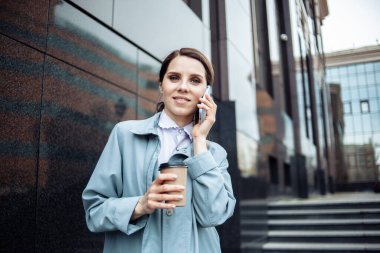 Modern gülümseyen iş kadını telefonda konuşuyor ve merdivenlerde kahve içiyor. Yaşam tarzı, iş konsepti