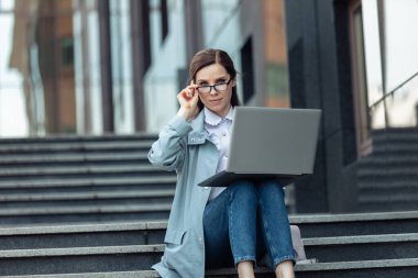 Beyaz tatlı kadın dışarıda merdivenlerde otururken dizüstü bilgisayar kullanıyor. Mesafeli iş. Modern iş kadını. Cihazlar kullanıyor. Yaşam biçimi 