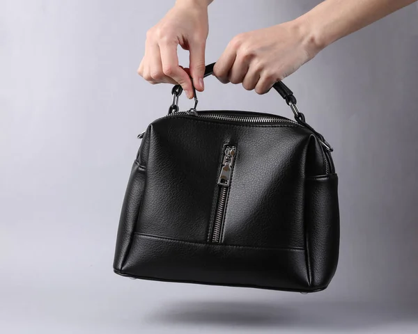 Woman\'s hand opens black leather bag on gray background