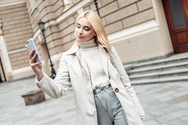 在城市里 年轻时髦的金发女人靠智能手机自拍 — 图库照片