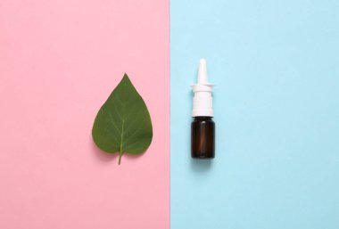 Mavi-pembe pastel arka planda burun spreyi ve yeşil yaprak. Burun akıntısı ve soğuk algınlığı tedavisi. Minimalizm