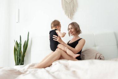 Sevgi dolu bir aile. Genç anne yatak odasında küçük kızıyla oynuyor. Anne ve bebek yatakta eğleniyor.
