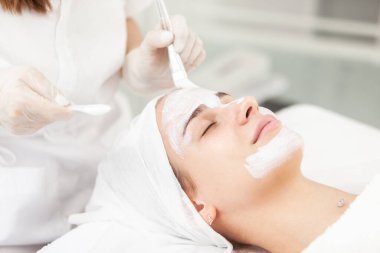 Güzellik uzmanı güzellik salonundaki güzel kadınsı yüze maske takıyor. Yüz temizliği, kozmetik prosedürleri, cilt bakımı, cilt gözenek temizleme, donanım kozmetolojisi konsepti